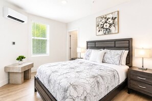 A bedroom with a bed, bedside tables, a nightstand, a potted plant, and a window with blinds.