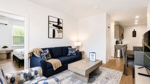 Un salon moderne avec un canapé, une table basse et un tapis. Il y a également un coin cuisine avec des placards et une table à manger.