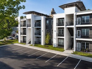A multi-story residential building with balconies, a parking lot, and a clear sky.