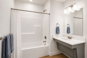 A bathroom with a bathtub, a shower curtain, a sink with a mirror, and towels. - Modern City Retreat- Walk to Convention Center (Hot Springs)