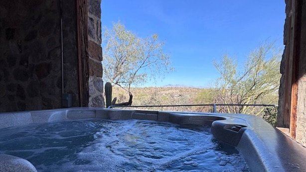 A hot tub with a stone wall and a clear view of trees and mountains.