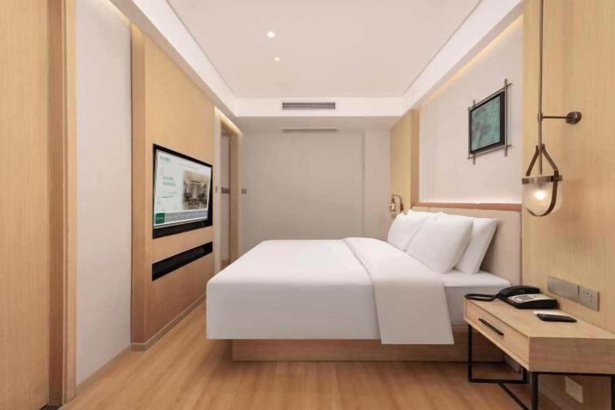 A modern hotel room with a bed, bedside table, and a mounted TV.