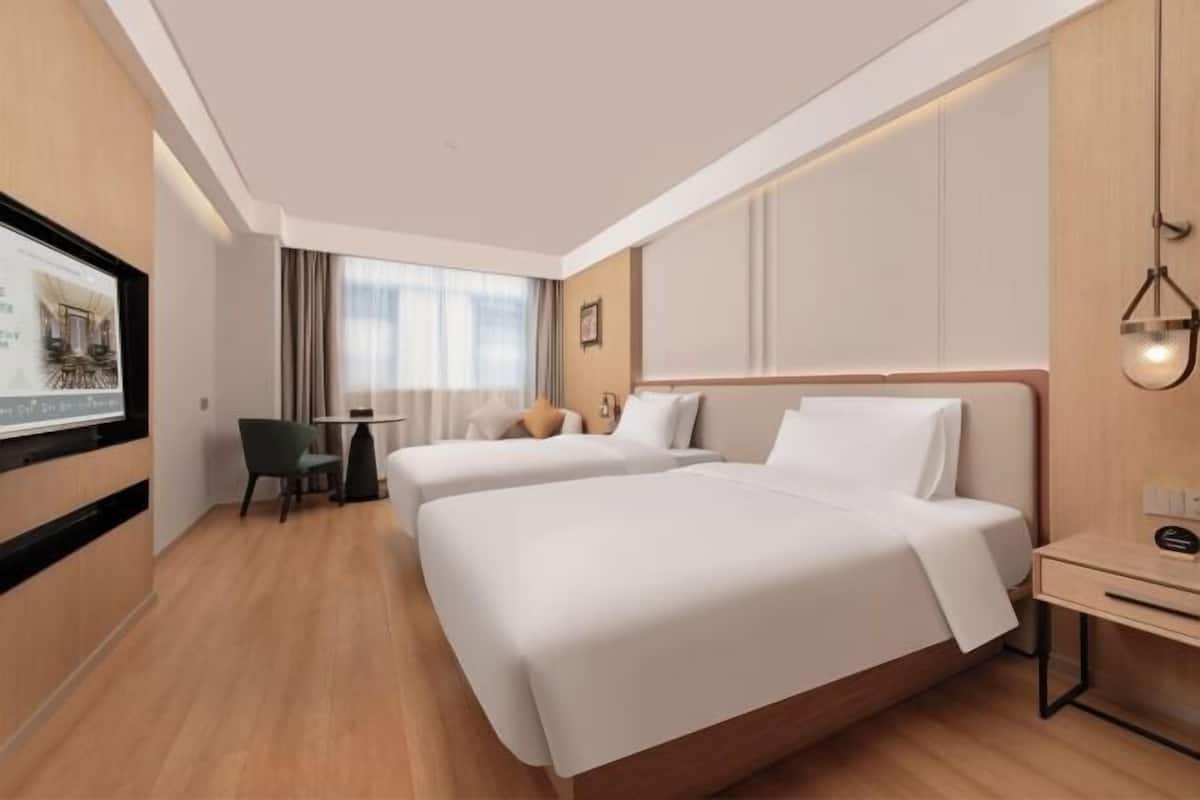 Quarto de hotel com duas camas, uma escrivaninha, uma cadeira e uma televisão na parede.