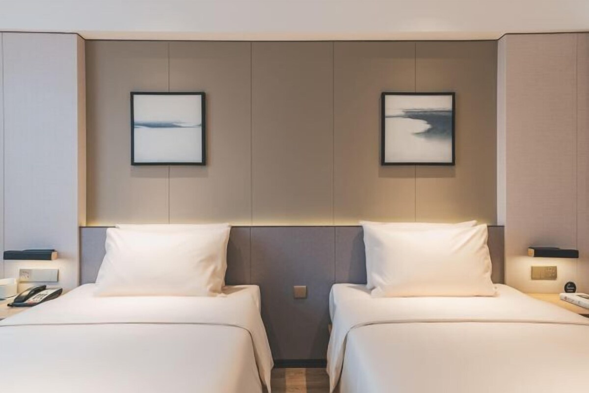 A hotel room with two beds, a nightstand with a phone, and a wall-mounted picture.
