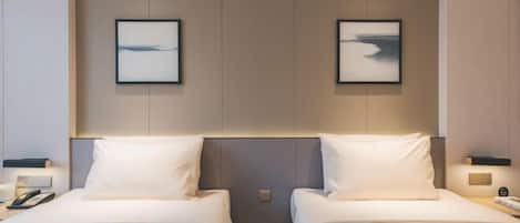 A hotel room with two beds, a nightstand with a phone, and a wall-mounted picture.