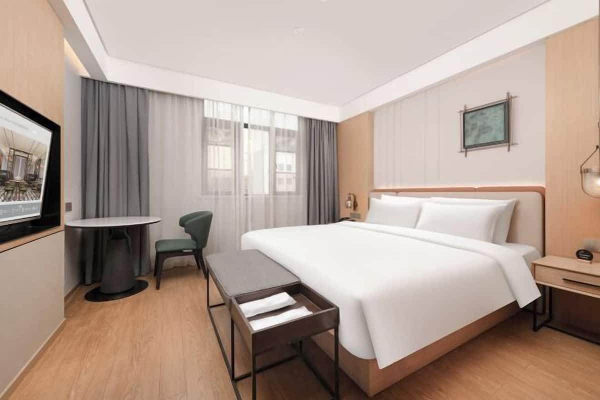 Quarto de hotel moderno com uma cama grande, uma escrivaninha pequena, uma cadeira e uma TV fixada na parede.