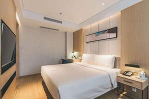 A modern hotel room with a large bed, a bedside table with a lamp, a flat-screen TV mounted on the wall, and a painting above the bed. - Meilun Hotel, Baymax Center, Dongting, Wuxi (Wuxi)