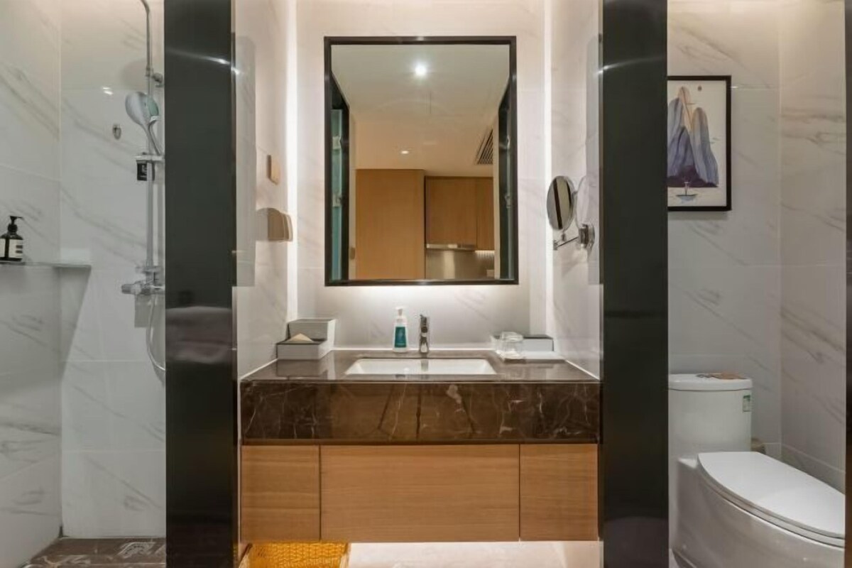 A modern bathroom with a marble vanity, a large mirror, and a toilet.