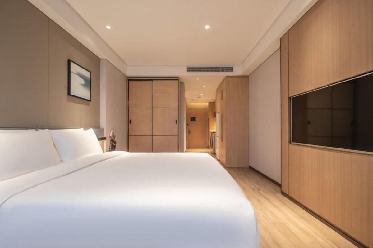 A modern hotel room with a large bed, wooden wardrobe, and a television.