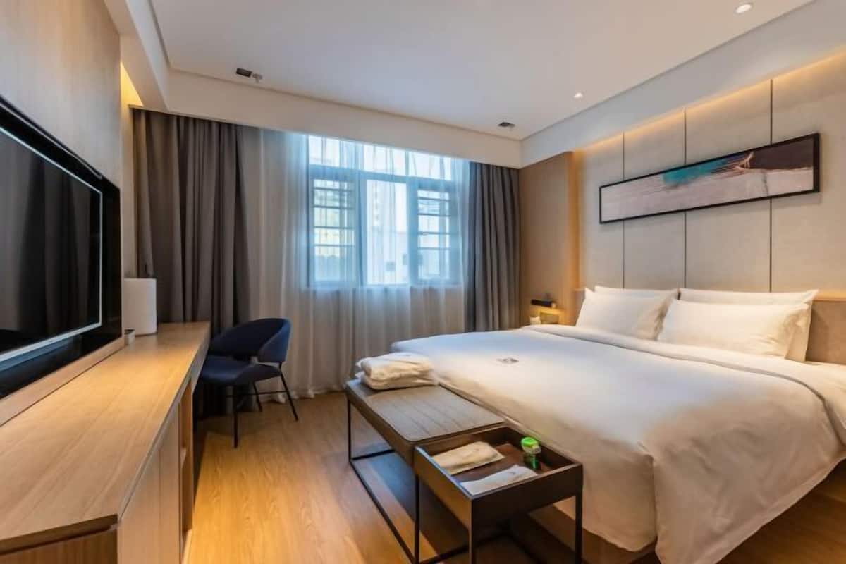 Quarto de hotel moderno com uma cama grande, uma escrivaninha com cadeira, televisão de tela plana e janela com cortinas.