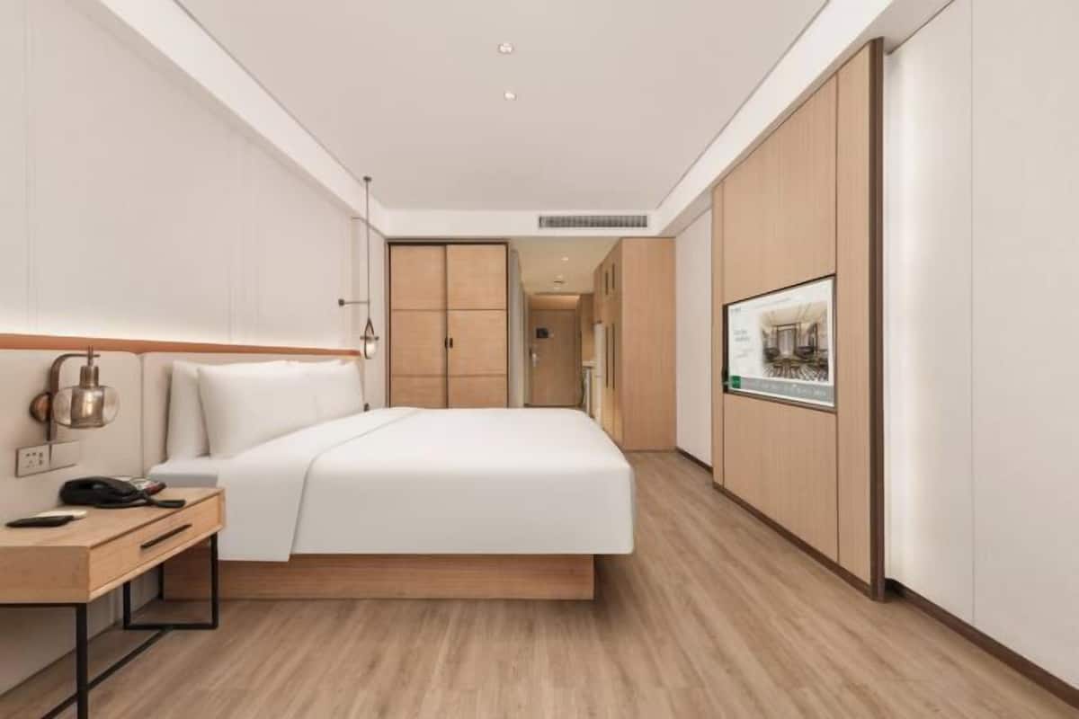 Quarto de hotel moderno com cama, mesa de cabeceira, abajur e um quadro na parede.