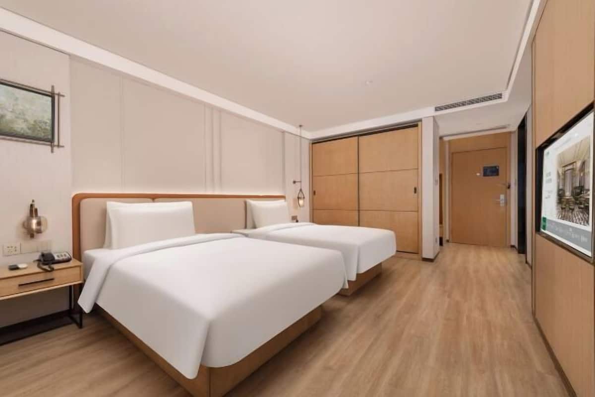 Quarto de hotel com duas camas, uma mesinha de cabeceira, uma luminária e um guarda-roupa.