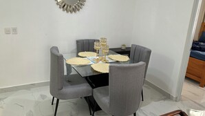 Un comedor con una mesa de vidrio, sillas tapizadas en gris y un espejo decorativo en la pared.