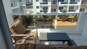 Balcón con sofá y mesa, con vista a un patio con palmeras y una piscina.