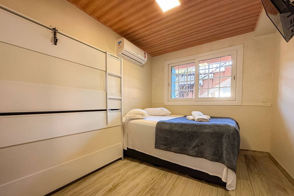 Um quarto com cama, janela com vista, ar condicionado e teto de madeira.