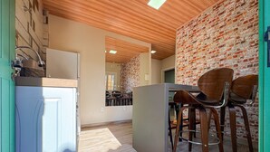 A kitchen with a wooden ceiling, a brick wall, and a dining area with wooden chairs. - Bella Serra Gramado Residence (Gramado)