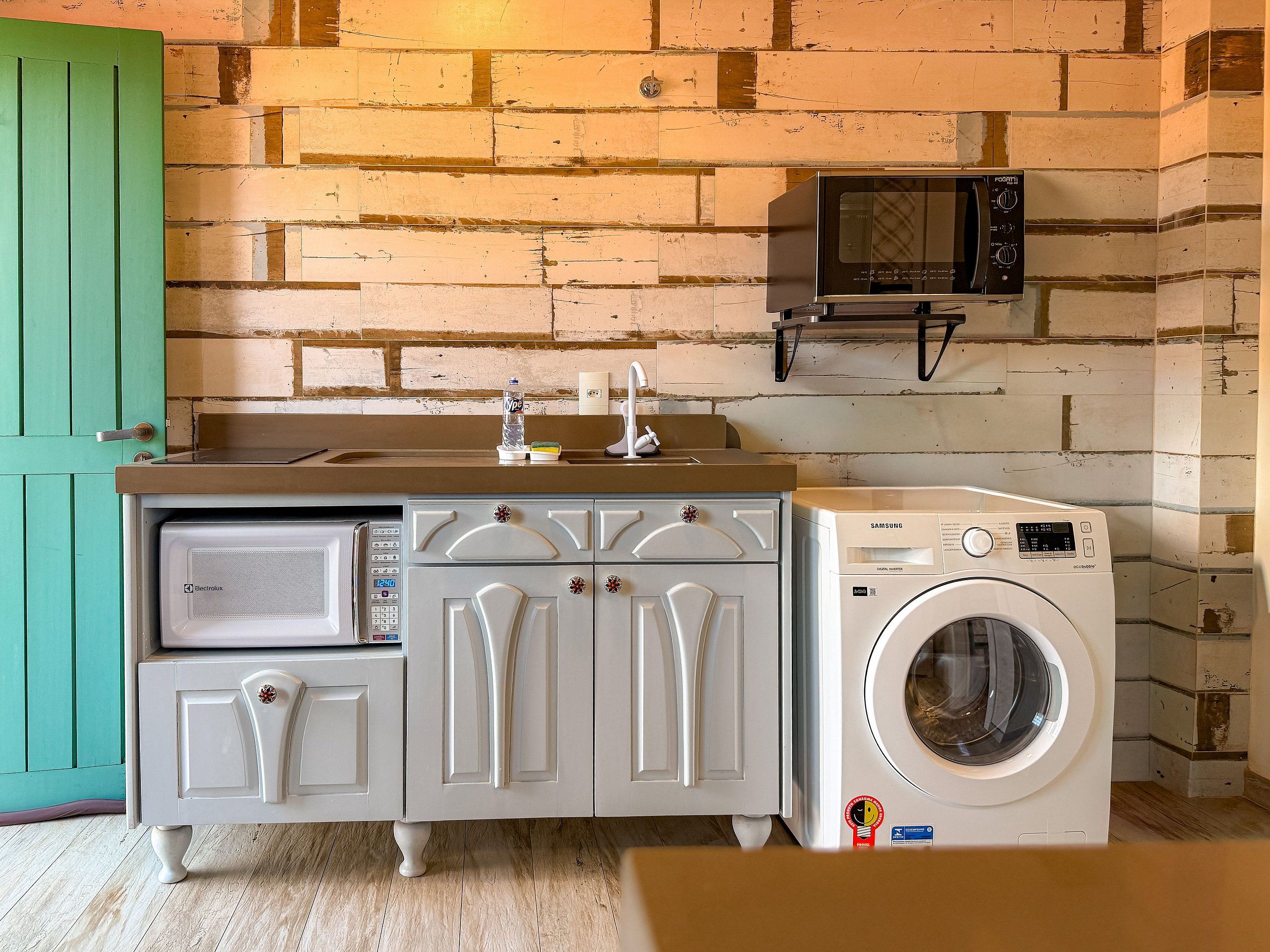 Una cocina compacta con microondas, lavadora y una puerta verde.