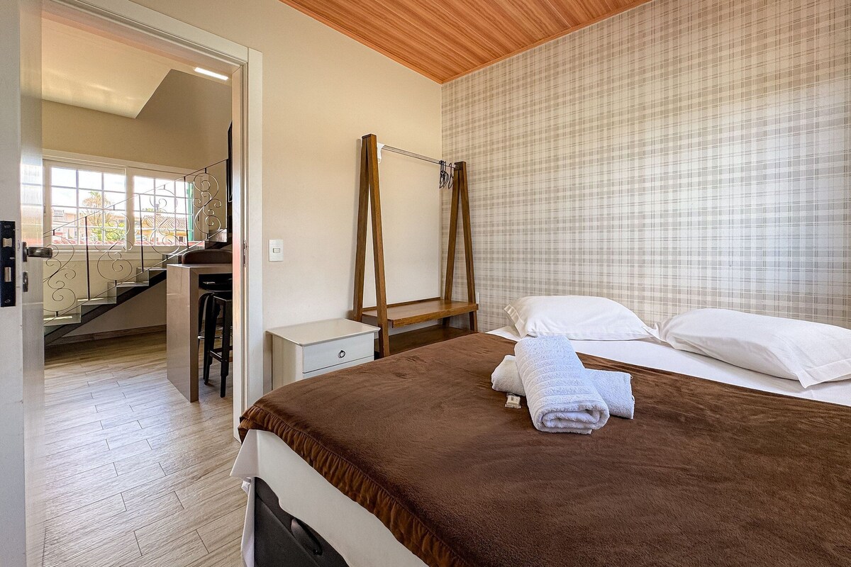 Quarto com uma cama, mesa de cabeceira, escada de madeira e vista para uma escadaria.