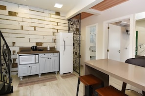 Una cocina con pared de madera, armarios blancos, un refrigerador y una cafetera.