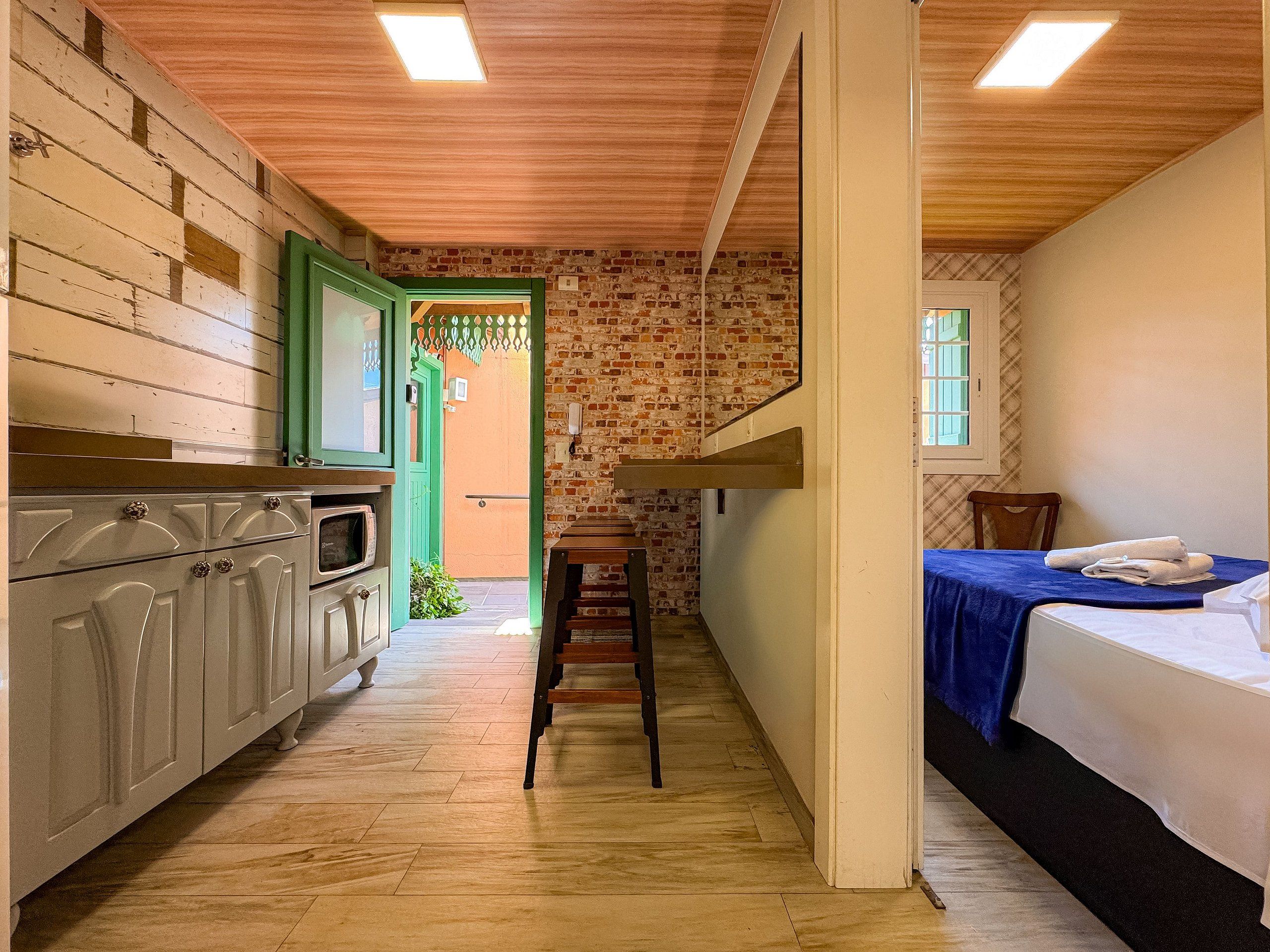 A narrow hallway with a kitchen on one side, a staircase, and a bed on the other.