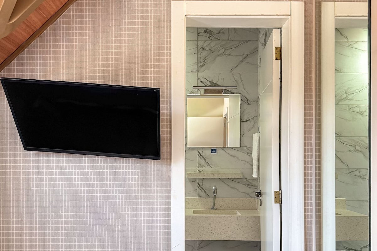 Quarto com cama, TV fixada na parede, banheiro com piso de mármore e escada com espelho.