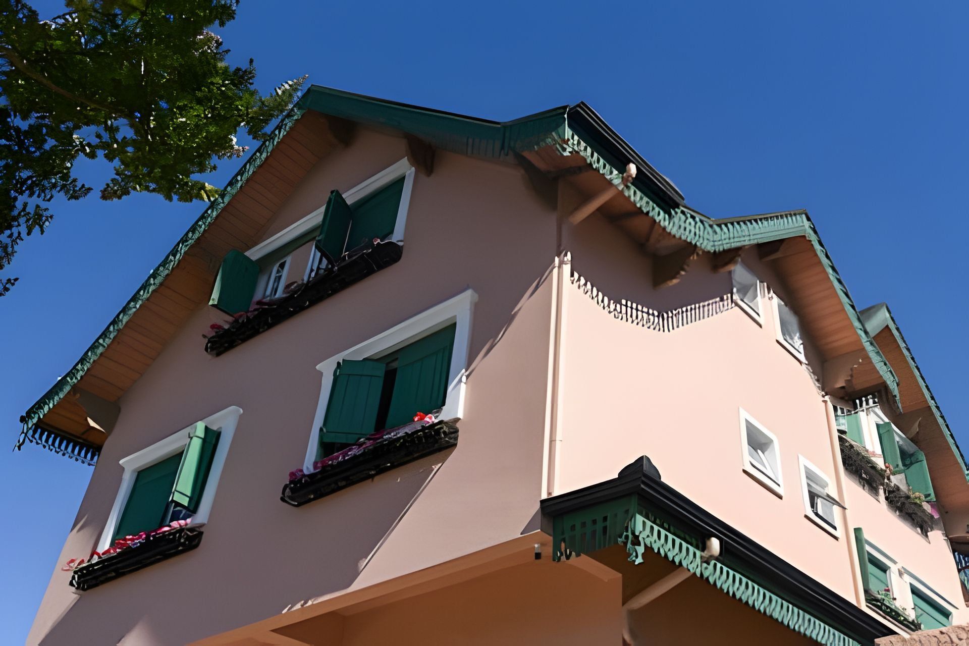 Um edifício com vários andares, varandas, persianas verdes e telhado inclinado.