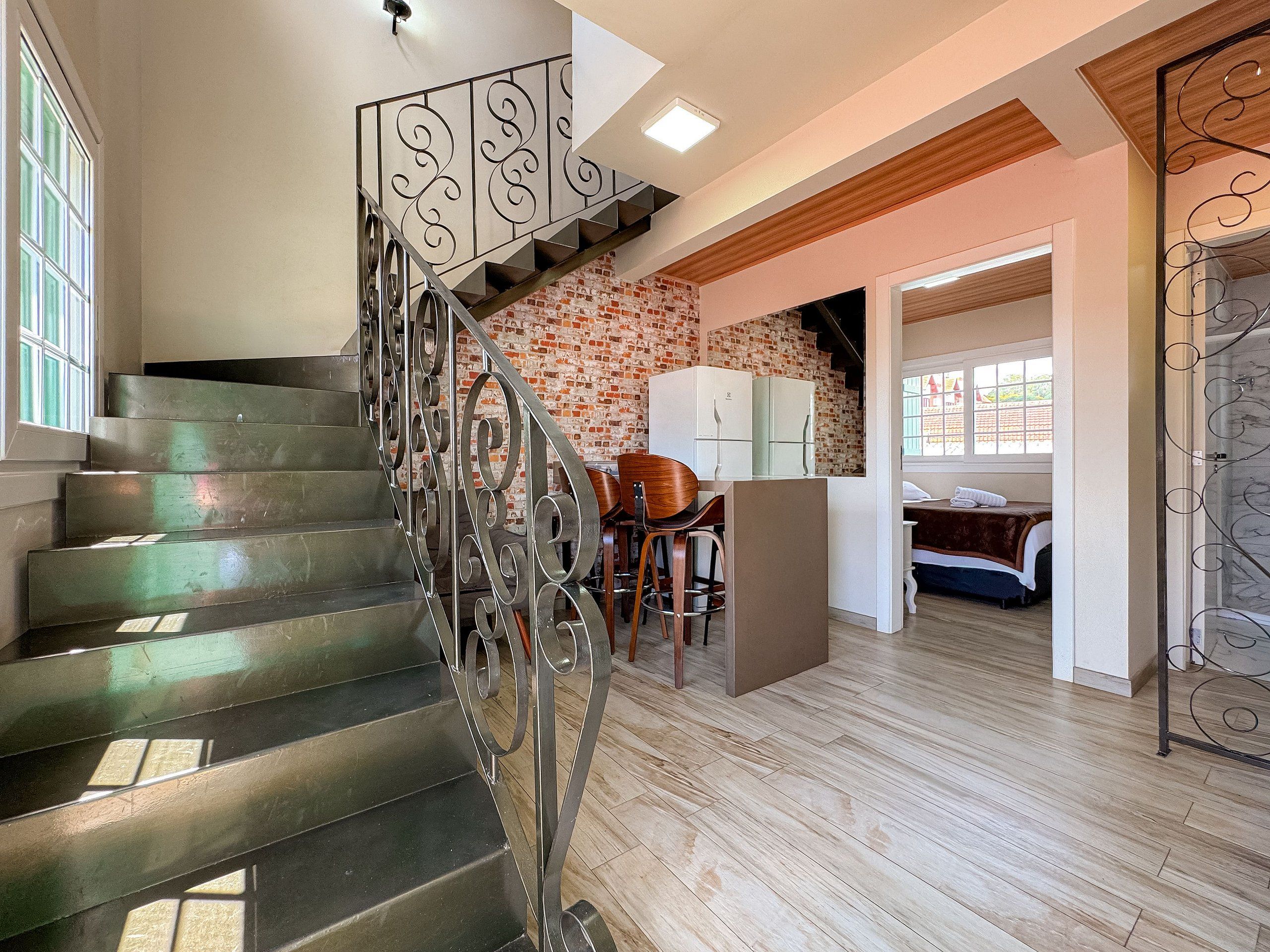 Un escalier avec des rampes en métal, un coin cuisine avec des meubles blancs et une chambre à coucher avec un lit et une fenêtre.