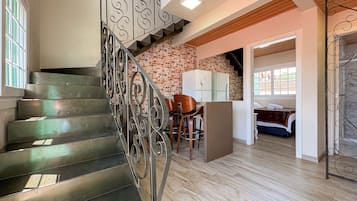 Un escalier avec des rampes en métal, un coin cuisine avec des meubles blancs et une chambre à coucher avec un lit et une fenêtre.