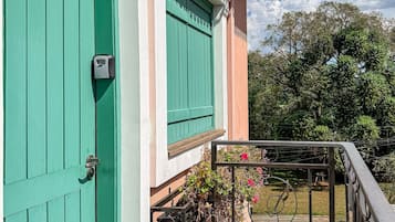 A turquoise door with a keypad lock, a balcony with a metal railing, and a garden with flowers.