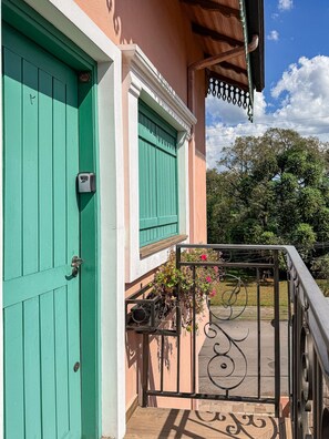 Une porte turquoise dotée d’un clavier pour l’ouverture, un balcon avec une rambarde en métal et un jardin fleuri.