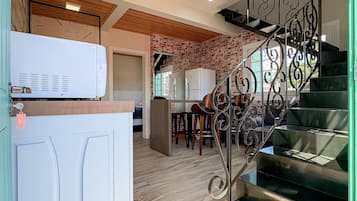 Uma cozinha com geladeira branca, armário de madeira e escada com grades de metal decoradas, que dá acesso a uma sala de jantar.