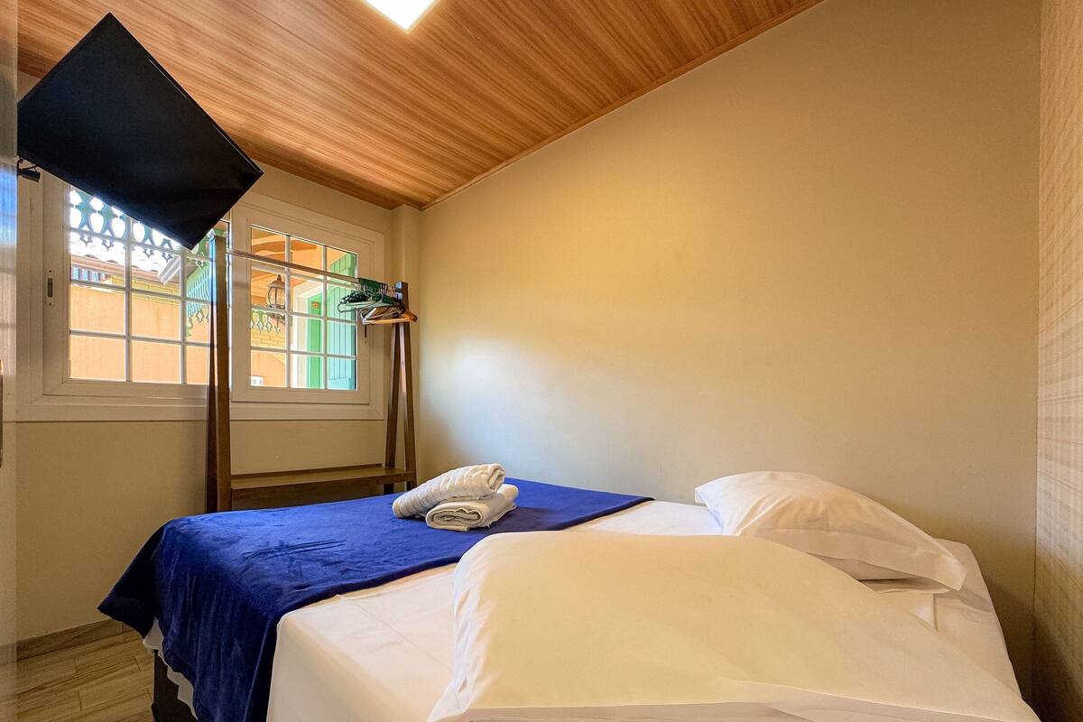 Quarto de hotel com cama, janela com vista, teto de madeira e um porta-toalhas suspenso.