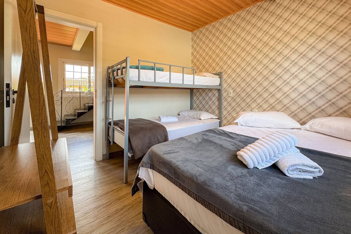 Quarto com beliches, uma escada de madeira, parede estampada e uma porta que dá para uma escadaria.