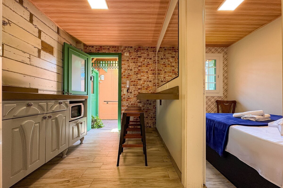 Um corredor estreito com uma cozinha de um lado, uma escada e uma cama do outro.