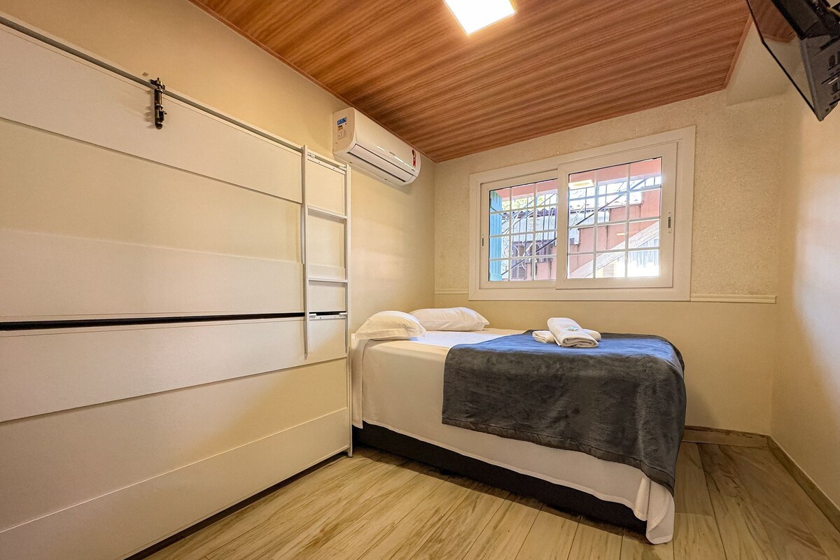 Um quarto com cama, janela com vista, ar condicionado e teto de madeira.