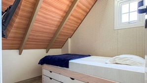 A bedroom with a sloped ceiling, a bed with a blue blanket, a window, and a wall-mounted air conditioning unit. - Bella Serra Gramado Residence (Gramado)