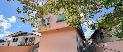 A building with a pink facade, green shutters, and a tiled patio area.