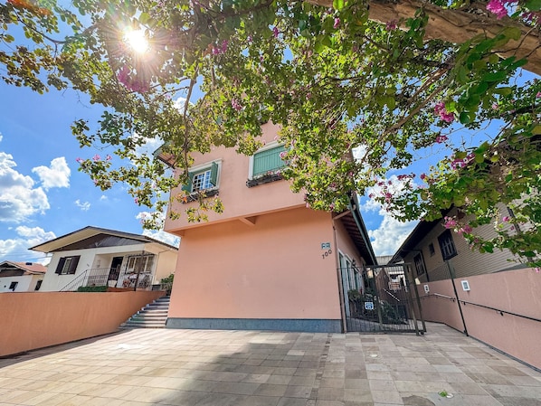 A building with a pink facade, green shutters, and a tiled patio area.