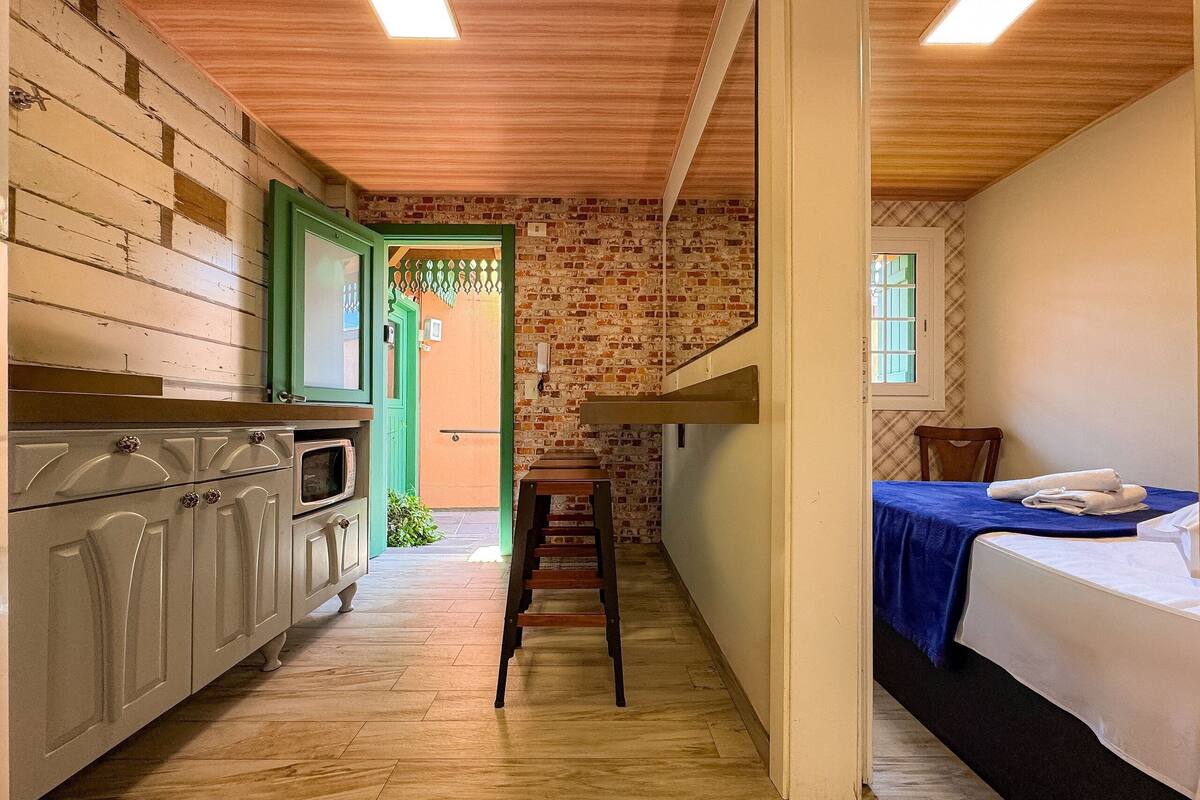 Um corredor estreito com uma cozinha de um lado, uma escada e uma cama do outro.