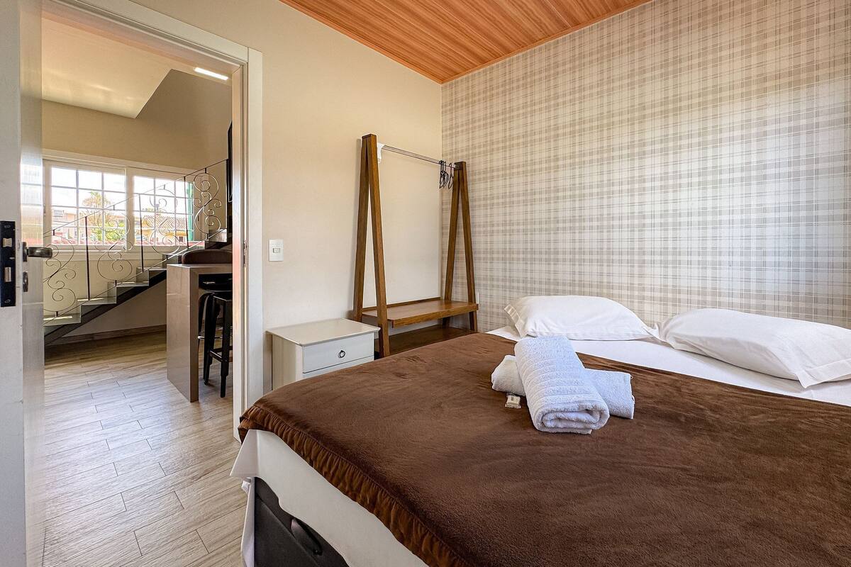 Quarto com uma cama, mesa de cabeceira, escada de madeira e vista para uma escadaria.