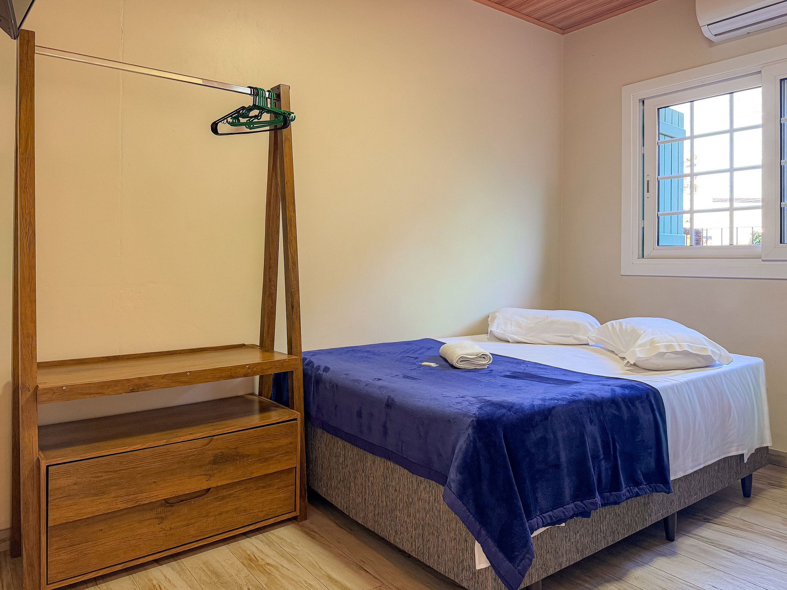 Un dormitorio con cama, armario de madera, ventana y lámpara colgante.