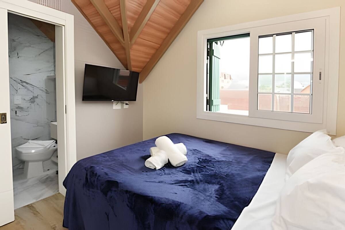 Quarto com cama, televisão, janela e banheiro.