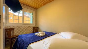 Un dormitorio con cama, ventana, televisor montado en la pared y una silla.