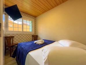 A bedroom with a bed, a window, a TV mounted on the wall, and a chair.