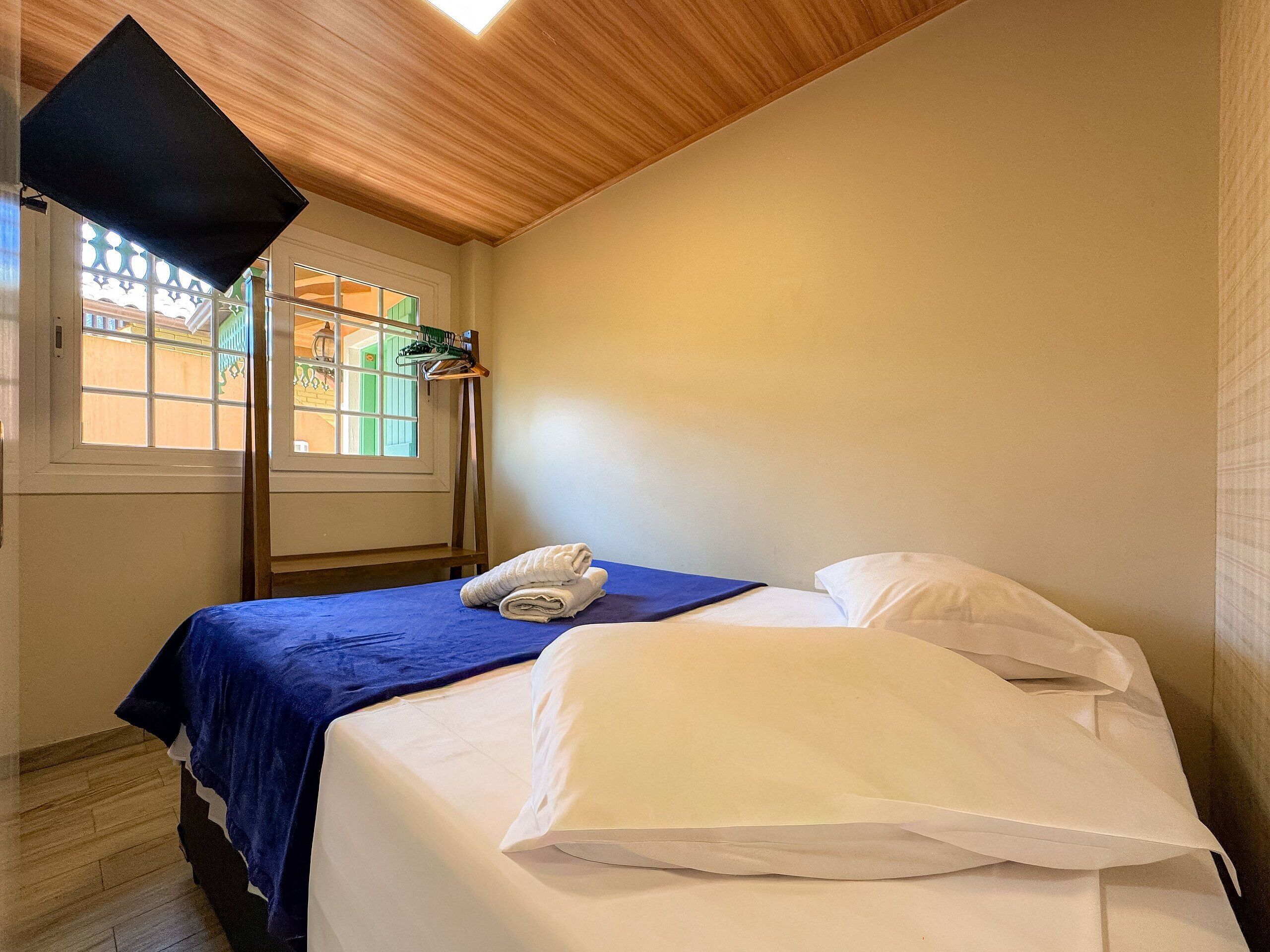Habitación de hotel con cama, ventana con vistas, techo de madera y toallero colgante.