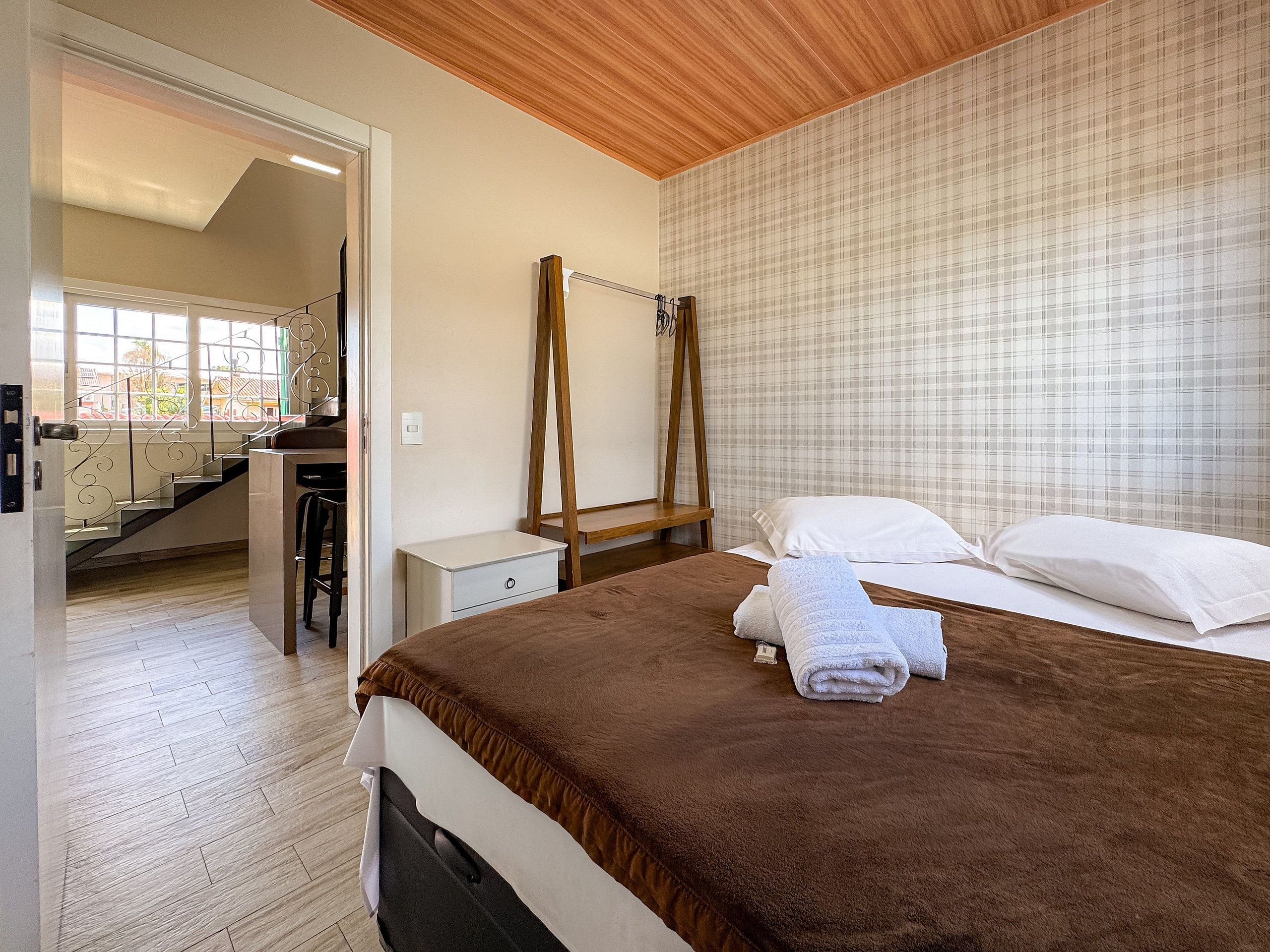 Quarto com uma cama, mesa de cabeceira, escada de madeira e vista para uma escadaria.