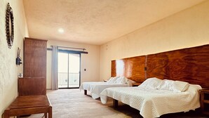 A hotel room with two beds, a wooden bench, a wardrobe, and a balcony.