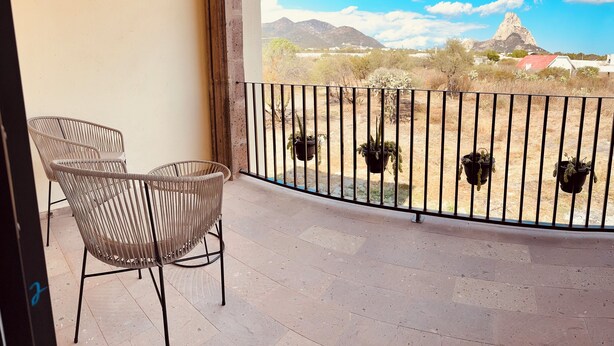 A balcony with two wicker chairs, a view of a mountain, and potted plants on the railing. - Hotel Suites Piamonte (Bernal)