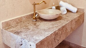 A bathroom with a marble sink, gold faucet, and a round mirror with a gold frame. - Hotel Suites Piamonte (Bernal)