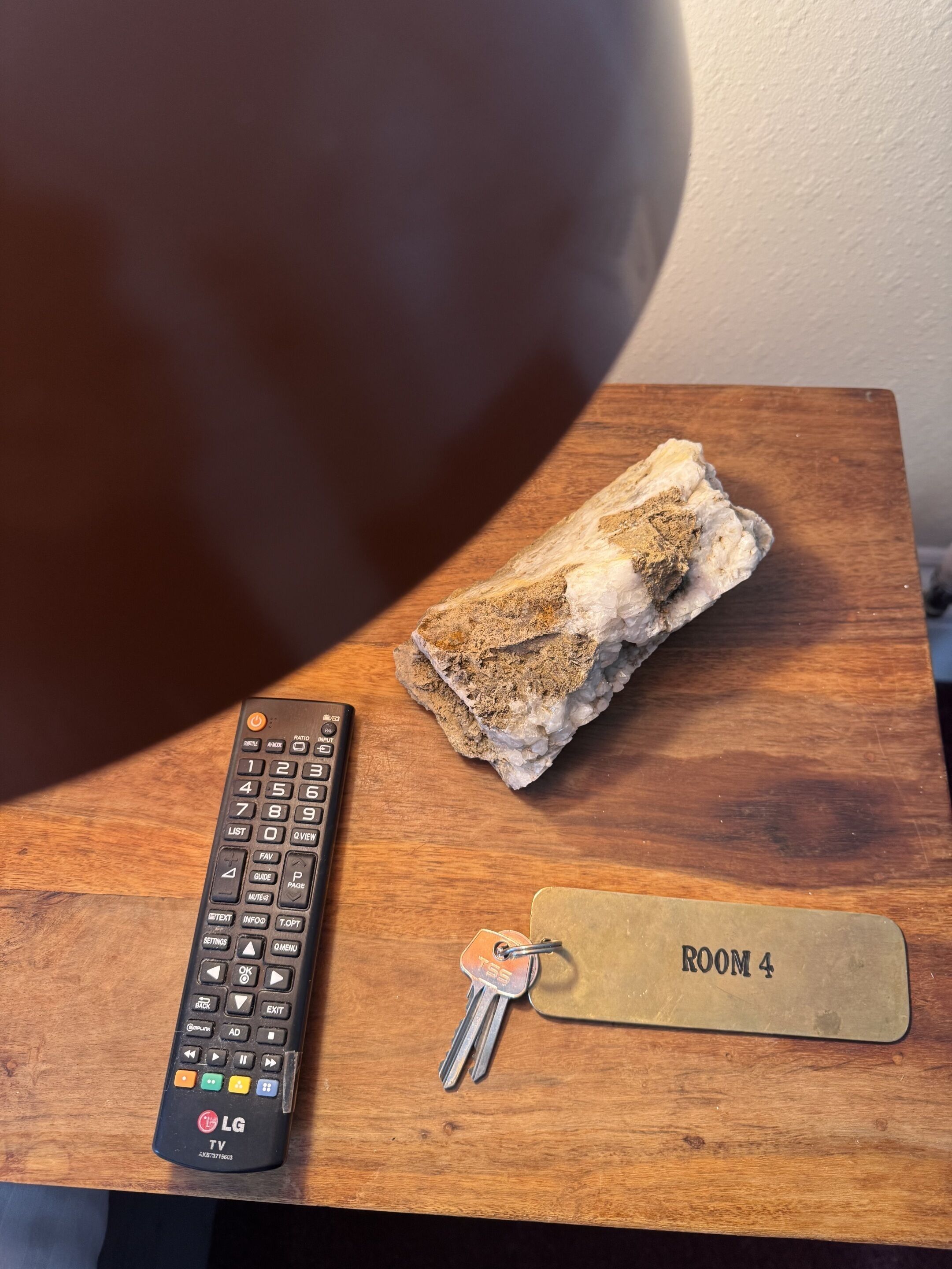 A remote control, keys, and a room key on a wooden surface.